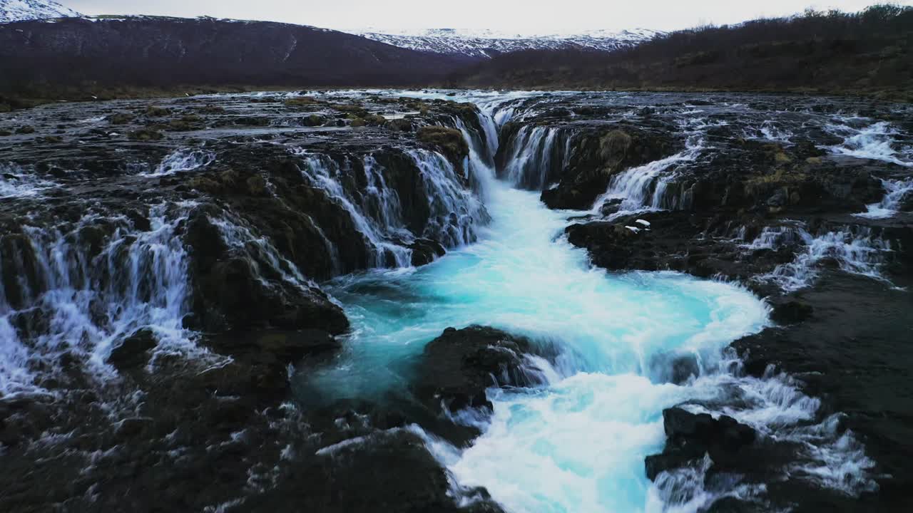 sobrevuelo aéreo hermosa agua glaciar de color azul del río que fluye y cae por la cascada de bruarfoss en islandia