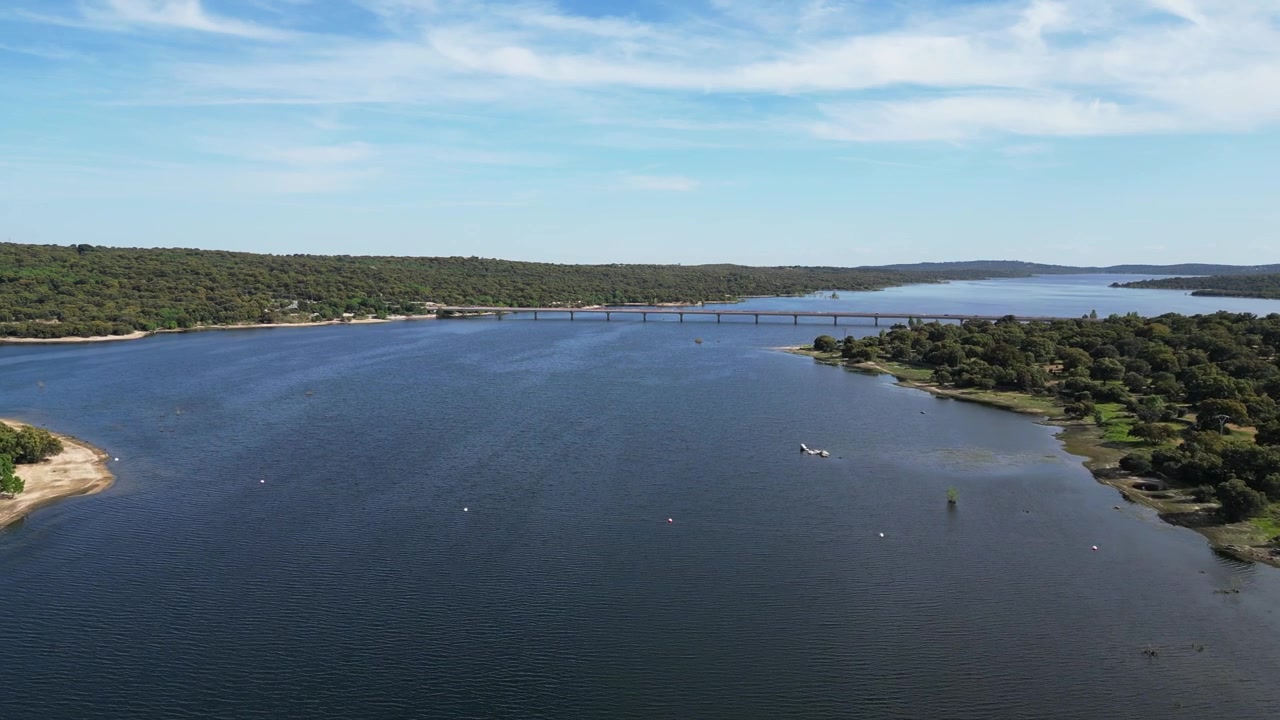 Un ampio corso d'acqua si estende verso un ponte lontano, circondato da una vegetazione lussureggiante. Ideale per documentari ambientali o servizi di viaggio.