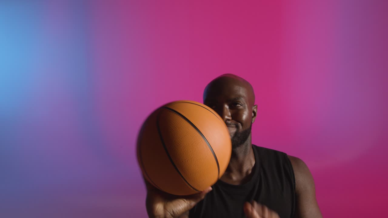 retrato de estudio de un jugador de baloncesto girando la pelota en el dedo contra un fondo iluminado de rosa y azul