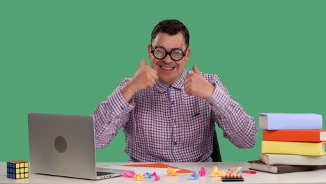 un hombre se sienta en un escritorio frente a una computadora portátil, piensa en algo, luego muestra un pulgar hacia arriba con ambas manos. retrato de un hombre con gafas en el estudio en una pantalla verde. cámara lenta.
