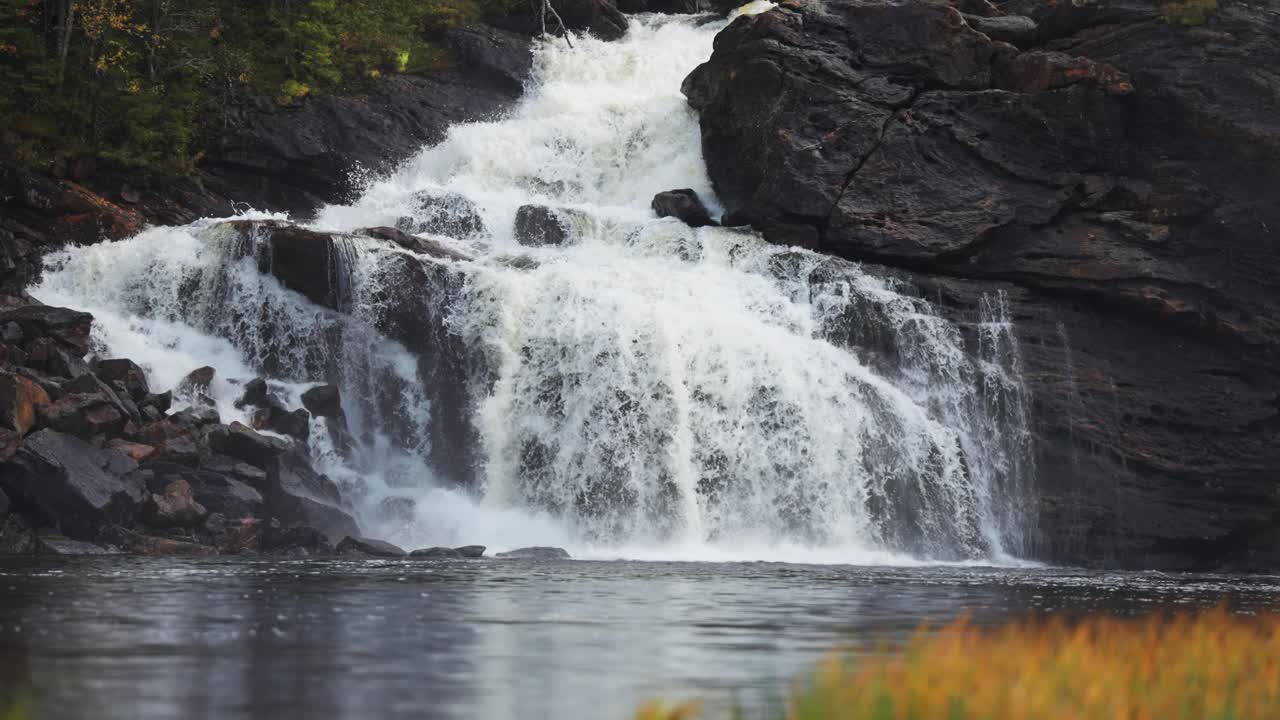 A waterfall cascades over the dark cliffs and is reflected on the surface of the lake