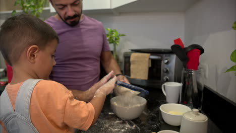 Zeitlupe-Eines-Kleinen-Mexikanischen-Lateinamerikanischen-Jungen-In-Jeans-Overalls,-Der-Mehl-Siebt-Und-Mit-Seinem-Vater-In-Der-Küche-Kekse-Backt