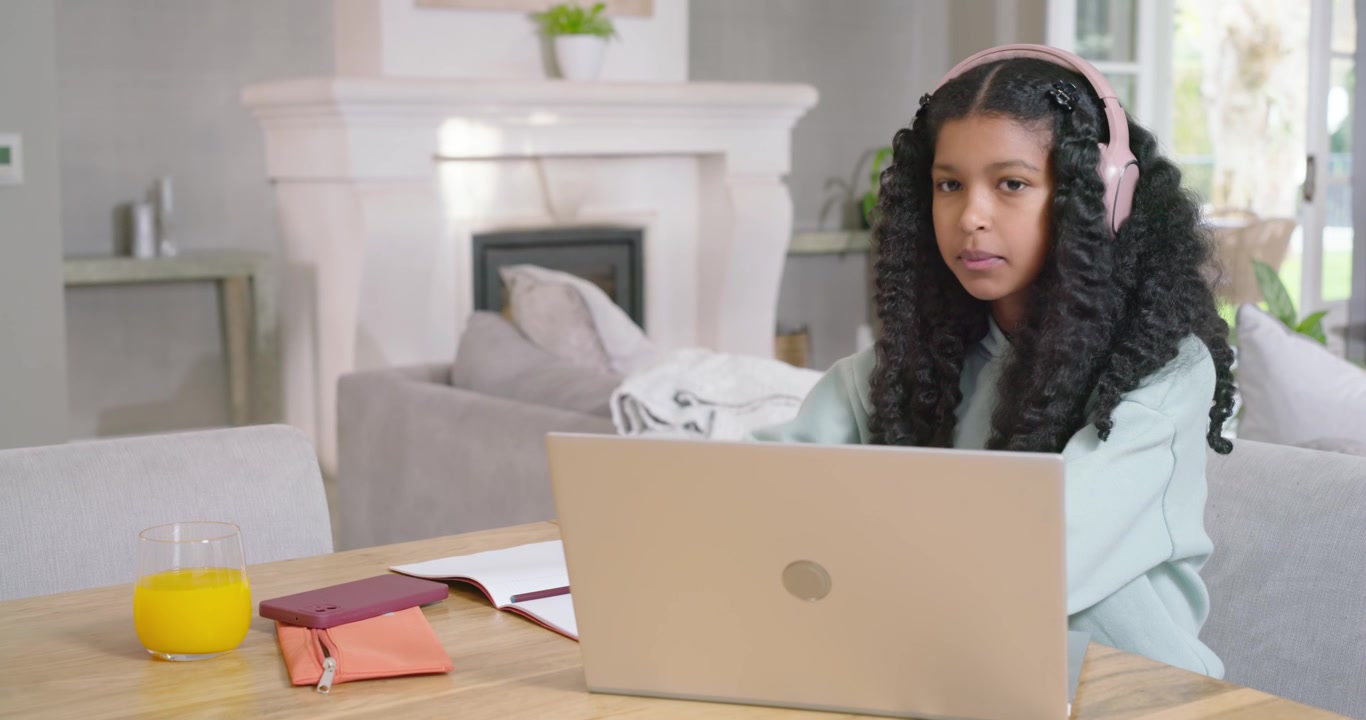 African American teen at table resting, with pink headphones, shifting laptop and notes, studying