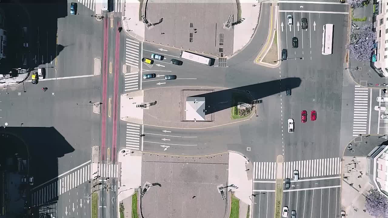High-angle view revealing dense traffic circling iconic buenos aires obelisk, showcasing urban movement across bustling metropolitan intersection during sunny daytime