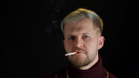 stylish addicted young man with blue eyes in trendy clothes looking at camera, smoking cigarette