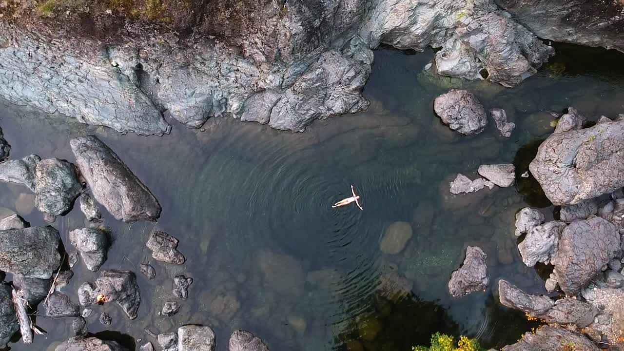 vista de pájaro de arriba hacia abajo, toma de drones de una chica en bikini flotando en aguas cristalinas en una piscina de rocas ubicada en el campo de la columbia británica, canadá