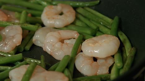 camera moving across hot pan with king prawns and fine beans cooking