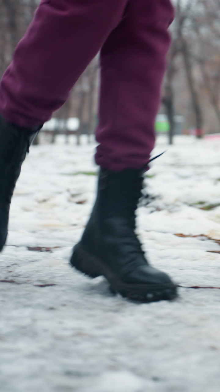 vista lateral de la pierna de una persona con botas negras corriendo en terreno nevado en un parque al aire libre, entorno urbano, clima frío, fitness en invierno, ejercicio en un entorno frío, entrenamiento de invierno