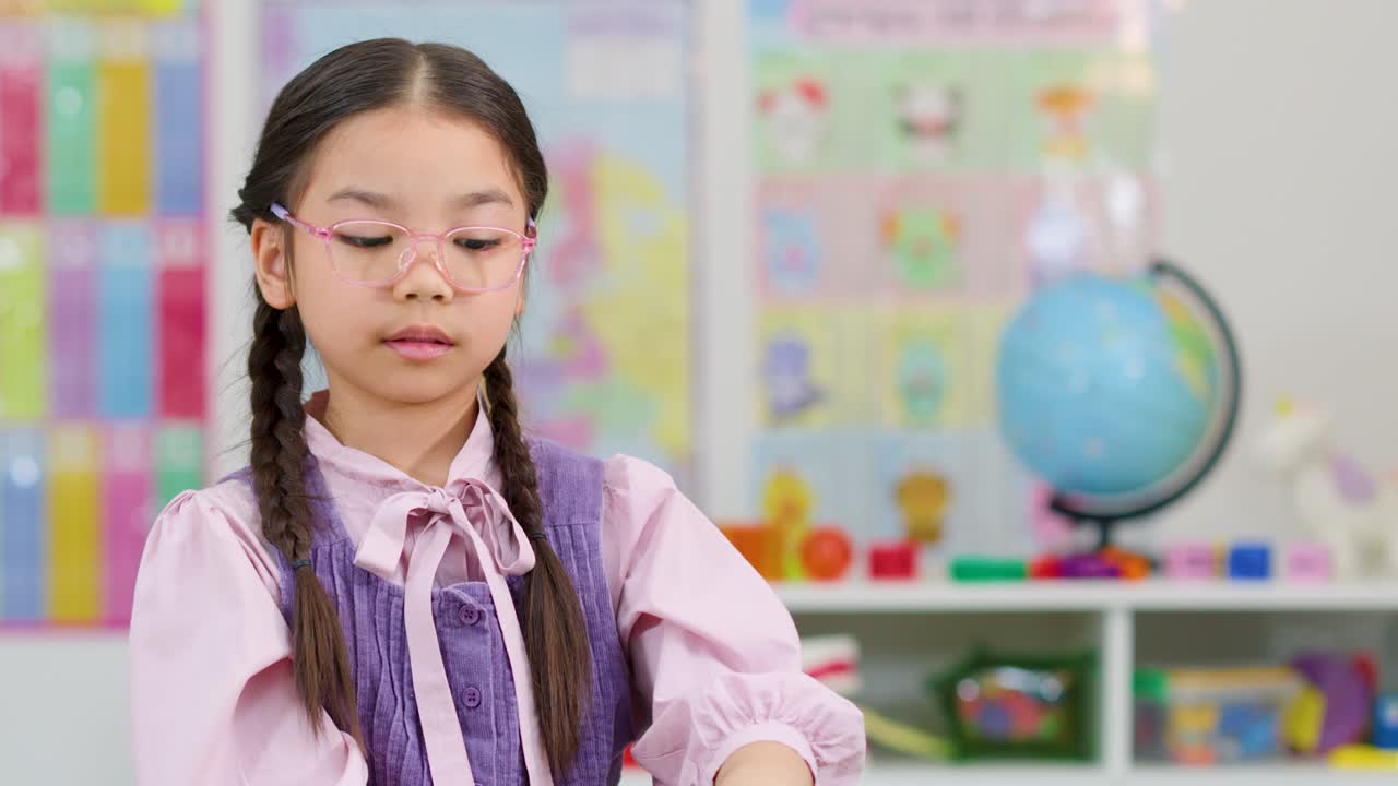 Smiling girl with glasses displays number five in bright classroom, soft lighting, static camera