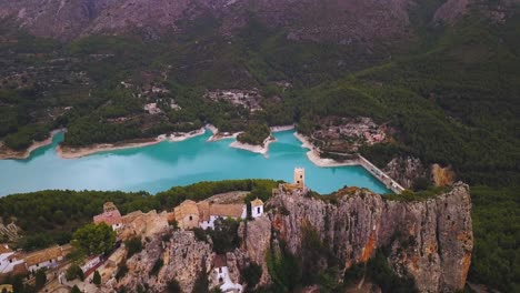 vista panorámica cinematográfica de drones 4k de la almena de un castillo medieval en la cima de un pueblo donde se observa un gran embalse de aguas turquesas