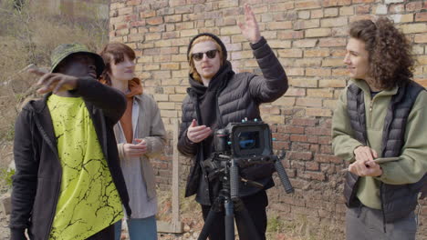 three production coworkers talking about a recording project and laughing in front of a camera on a tripod in the street while another worker taking notes