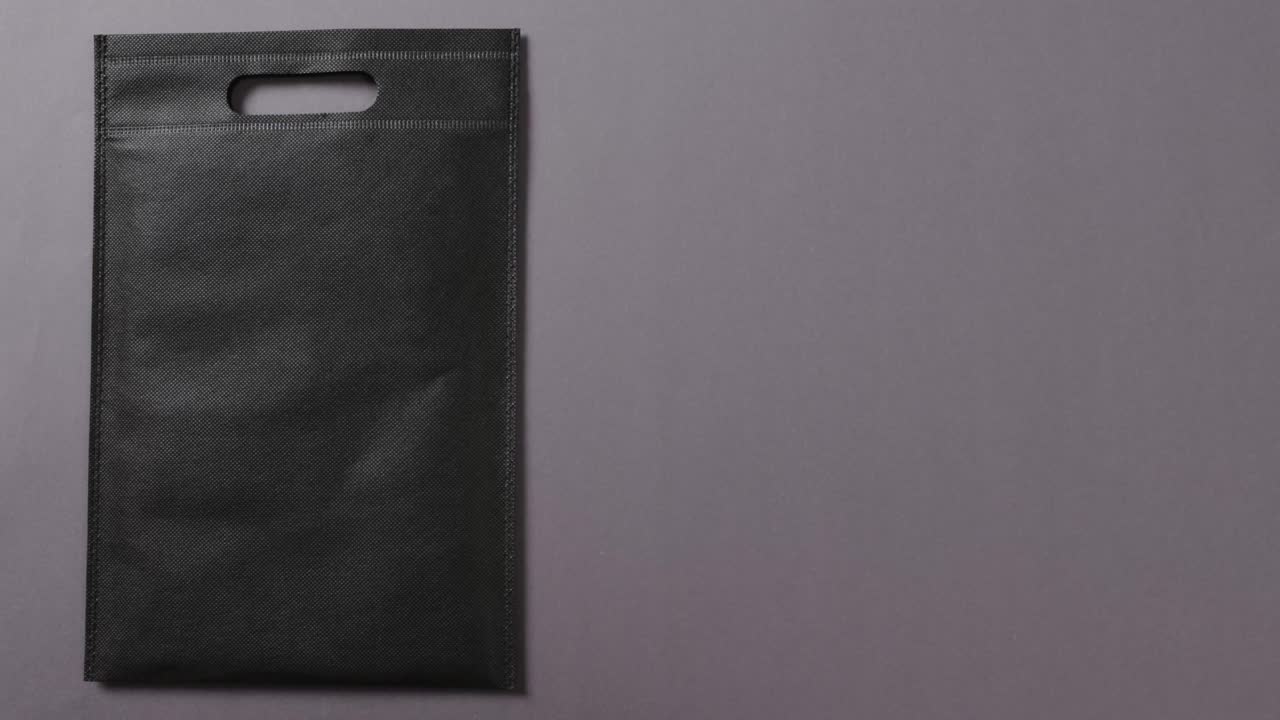 Primo piano di borsa nera su sfondo grigio, spazio per il testo, slow motion