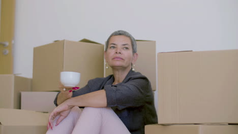 mujer sentada en el suelo, bebiendo té después de mudarse a una casa nueva