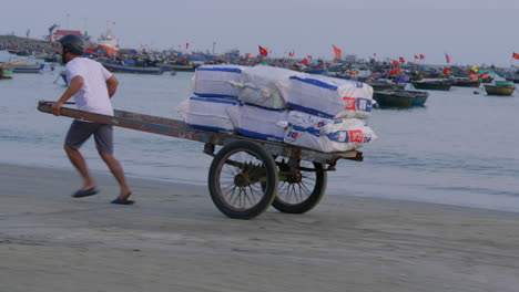 tracking shot of a delivery driver running with a hand cart carrying the goods along the beach