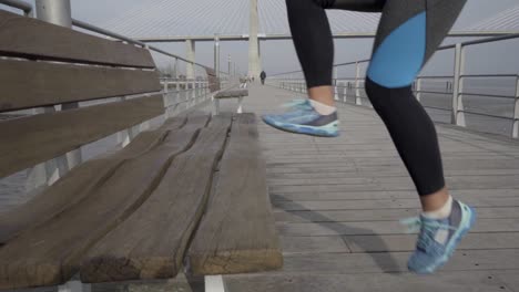 Cropped-shot-of-young-woman-training-near-wooden-bench-on-pier