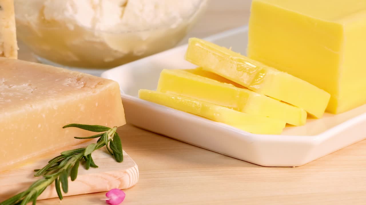 A close-up view of cheese wedges and butter slices garnished with rosemary on a wooden surface.