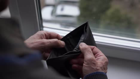 persona anciana jubilada abre y cierra la vieja billetera vacía