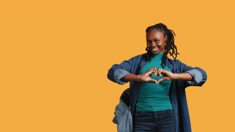 Portrait-of-affectionate-smiling-woman-doing-heart-symbol,-studio-background