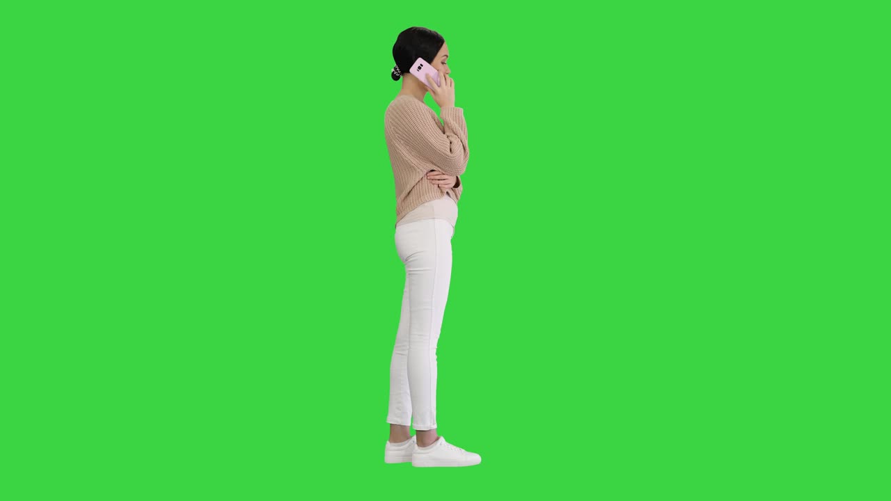 Giovane donna sorridente ed emozionata che parla al telefono e gesticola su schermo verde, chroma key