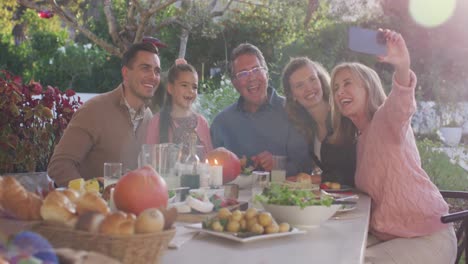 Video-of-happy-caucasian-parents,-daughter-and-grandparents-taking-selfie-at-outdoor-dinner-table