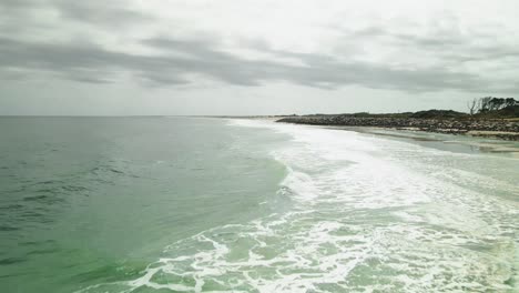 Waves lapping on shoreline of Kure Beach low aerial shot