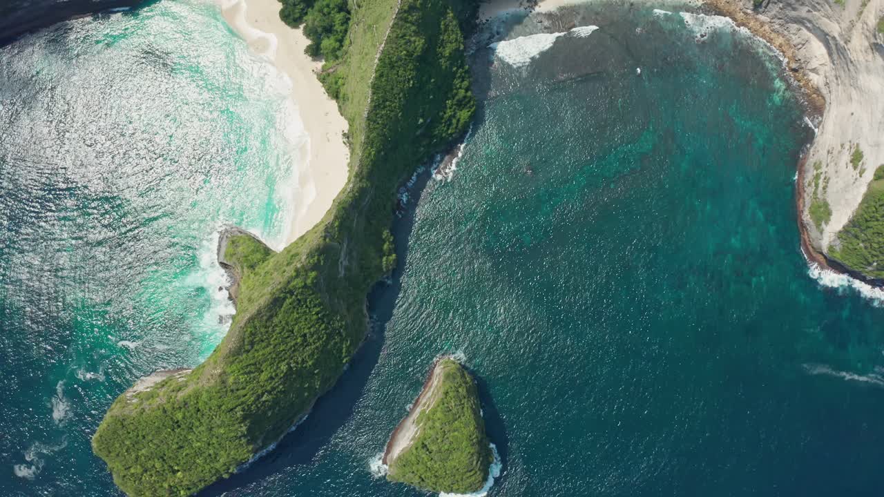 Aerial drone shot in the iconic Kelingking Beach, the 'T-Rex' shaped headland, and the towering limestone cliffs of Nusa Penida. Turquoise Indian Ocean crashes against the rocks and white-sand beach