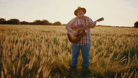 man singing and playing guitar in a wheat field at sunset