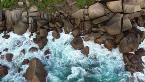 Bird-eye-drone-shot-of-north-east-point-beach,-huge-rock-boulders,-rough-sea,-waves-crushing,-Mahe-Seychelles-60fps