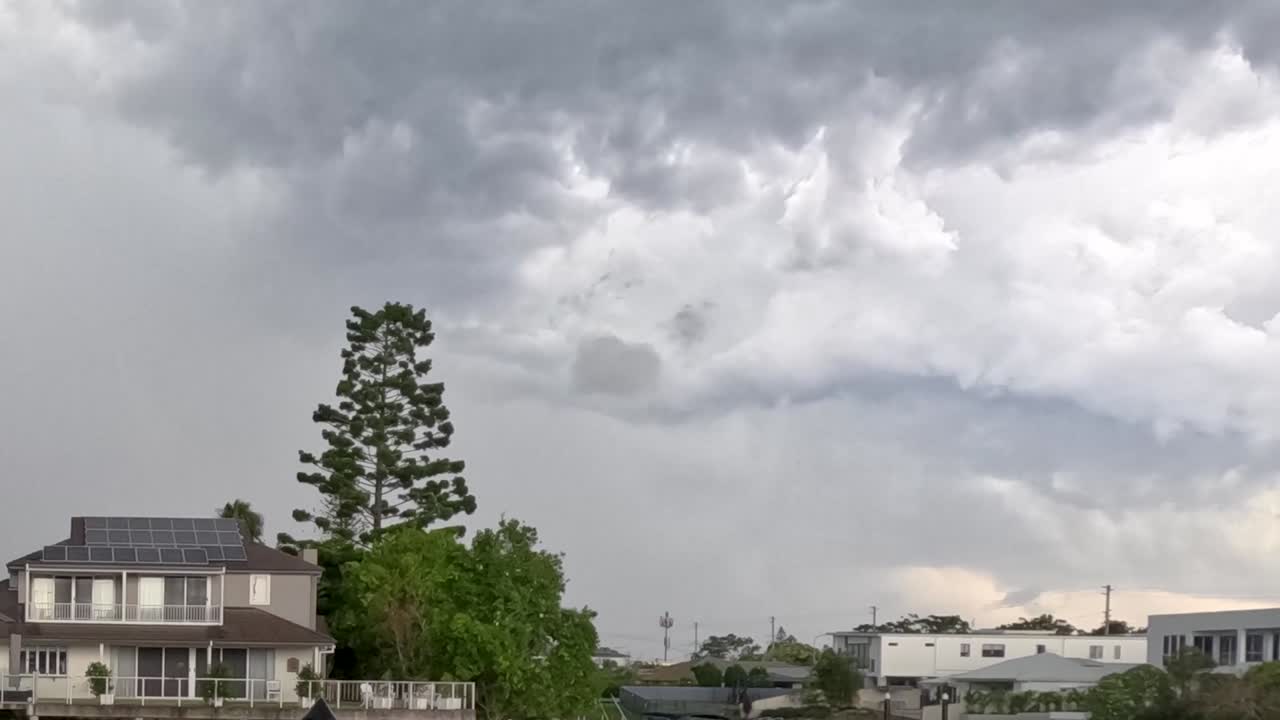 Ominous clouds gather above suburban houses, creating a dramatic and moody atmosphere.