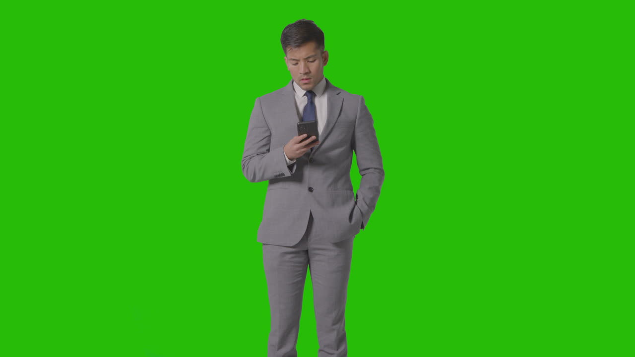 colpo in studio di uomo d'affari frustrato in giacca e cravatta contro lo schermo verde guardando il telefono cellulare 1