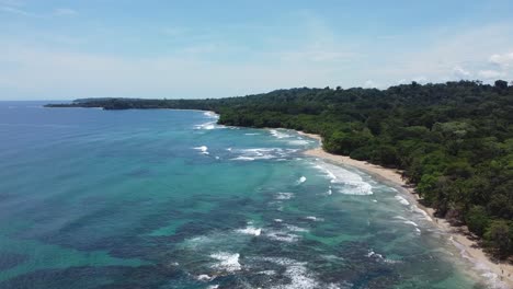 PUERTO-VIEJO,-COSTA-RICA---January-18,-2023:-flying-over-the-beach-,-with-a-forward-rise-movement-showing-the-lush-forest,-the-sand-and-the-sea