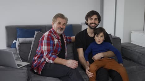 portrait of happy caucasian three generation men smiling to the camera at home, sitting on sofa