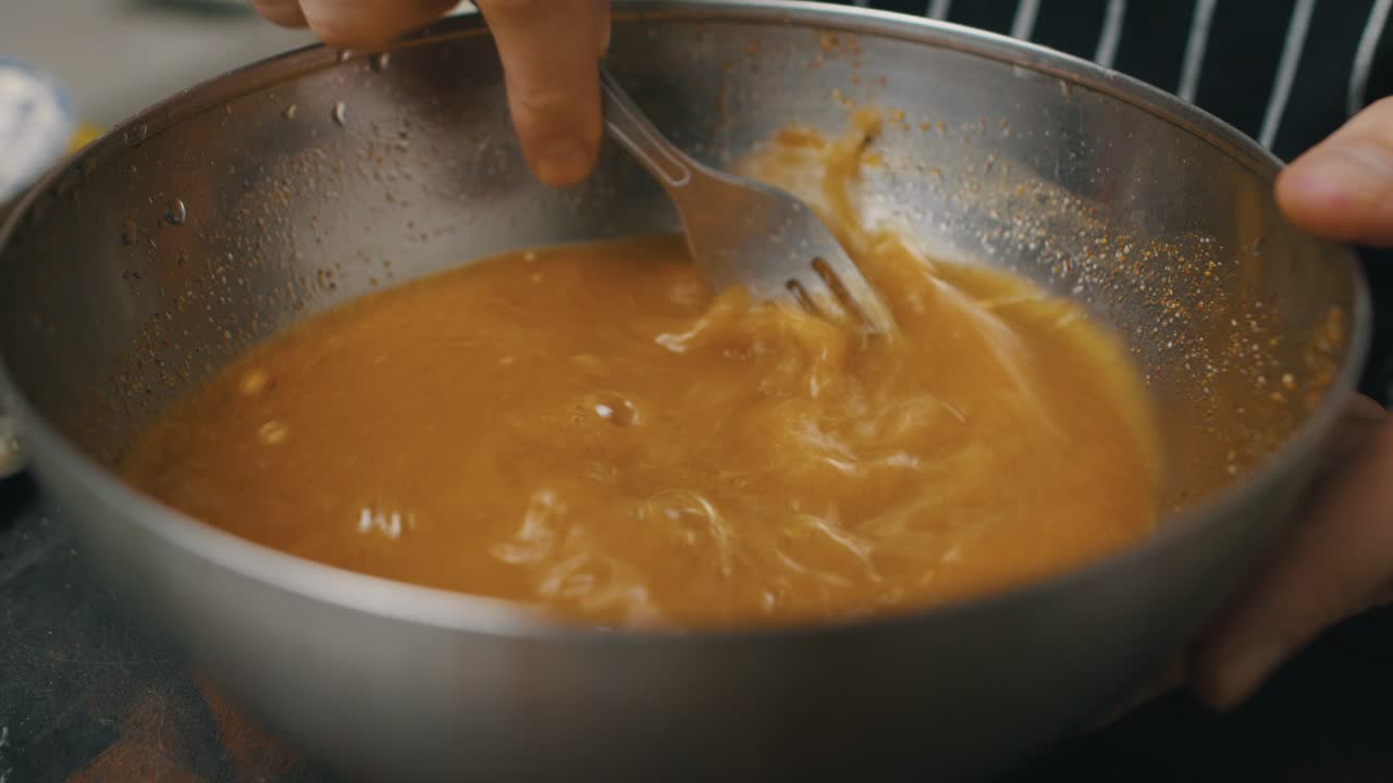 Stirring chicken meat sauce with fork inside deep metal cooking bowl