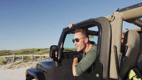 happy caucasian man in sunglasses getting out of car on sunny day at the beach