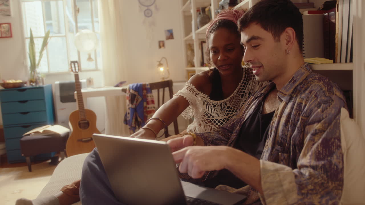 Young Couple Sitting on Bed and Discussing Something on Laptop