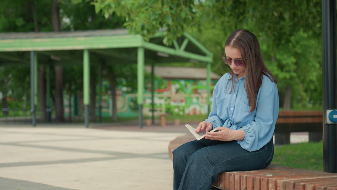 Donna studia all'aperto, signora caucasica rivede appunti all'esterno, donna in denim legge documenti di ricerca in un parco cittadino, si concentra sui suoi appunti di ricerca mentre è seduta in un parco urbano alberato