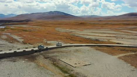 Aerial-drone-of-vans-carrying-cargo-and-tourists-crossing-a-bridge-in-the-high-altitude-alpine-plain-of-Deosai-National-Park-located-between-Skardu-and-Astore-Valley-in-Pakistan-on-a-sunny-summer-day