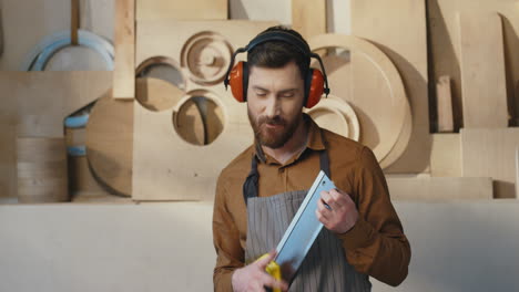 cheerful young caucasian carpenter in headphones having fun and playing with saw as if it were a guitar