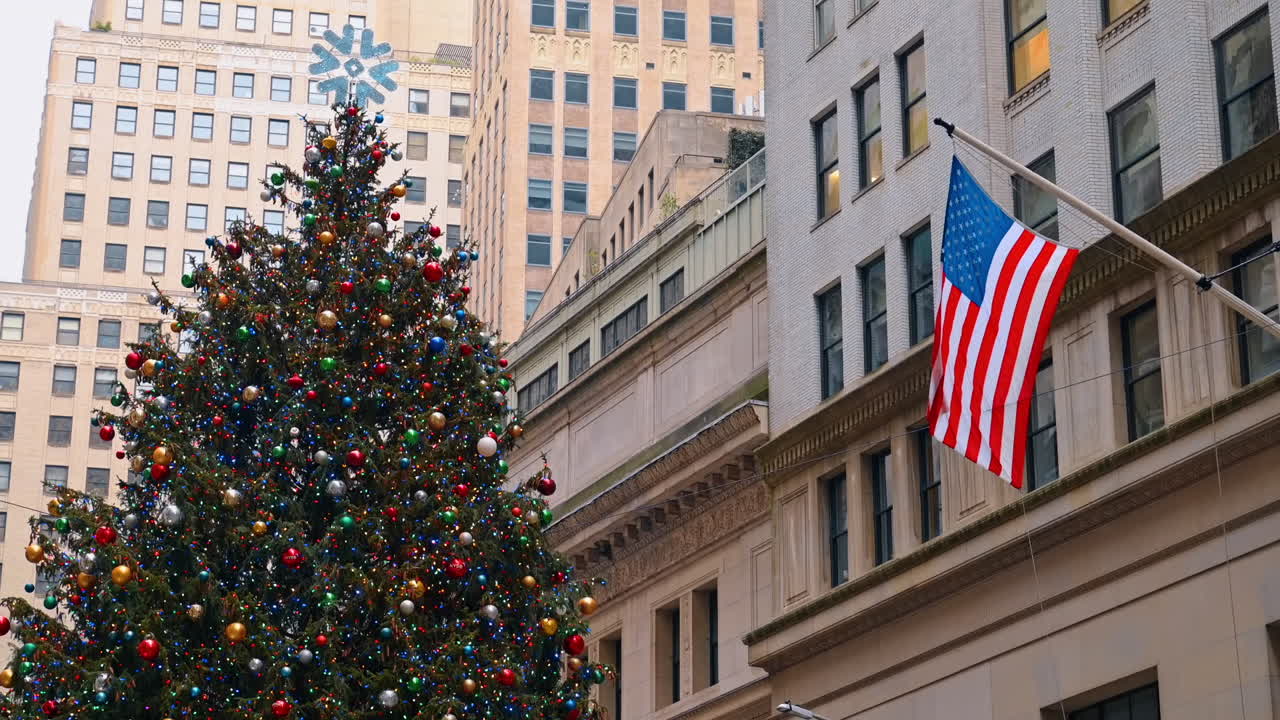Diverse palline colorate decorano un grande albero di Natale. Una bandiera americana è appesa sulla facciata dell'edificio.