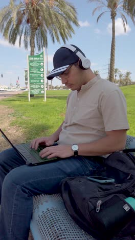 a man is sitting on a bench typing on a laptop at park, remote work.