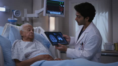 A doctor shows a patient brain scans on a tablet in a hospital room