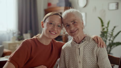 portrait of smiling young woman embracing elderly grandmother at home