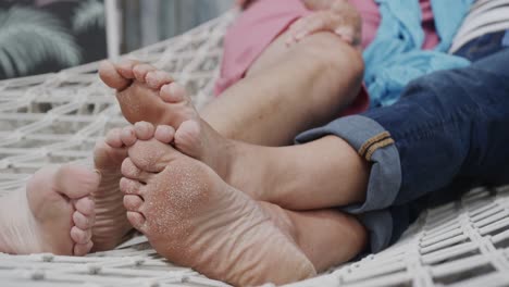 bare feet of happy senior caucasian couple lying together on hammock at beach bar, in slow motion