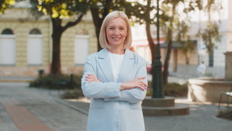 Happy mature caucasian businesswoman lady standing arms crossed looking at camera on city street