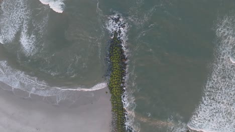 Aerial-drone-top-down-shot-over-stack-of-stones-bathed-in-the-beautiful-sea-water-along-the-sea-shore-at-daytime