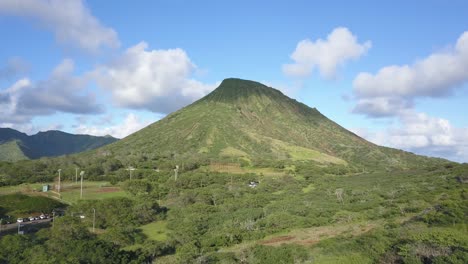 Aerial-dolly-rise-of-a-large-mountain-in-Hawaii-Kai-Honolulu-on-a-blue-sky-day-with-fluffy-clouds-and-a-baseball-field-in-view