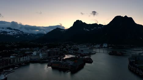 backward ascending drone reveals svolvaer city, sea, bridge and mountains in bright midnight sun
