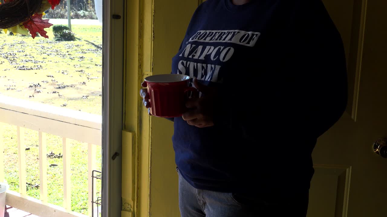 manos solamente- mujer afroamericana mirando por la puerta principal con una taza roja de café