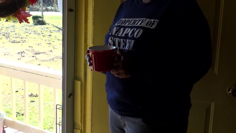 hands only- african american woman looking out front door with a red mug of coffee