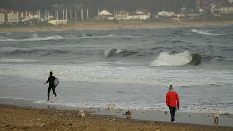 Surfer-running-along-the-tide-line-exited-for-surfing-at-Roker-beach-in-the-north-east-of-England-on-an-overcast-day